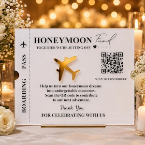 May include: A rectangular white acrylic sign featuring the text HONEYMOON FUND, TOGETHER WE'RE JETTING OFF, and a gold airplane icon. It includes a QR code with the text SCAN TO CONTRIBUE, along with instructions to contribute to a honeymoon.