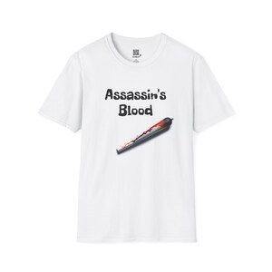 May include: White t-shirt with the text "Assassin's Blood" above a graphic of a bloody blade. The blade is a dark gray color with red and orange accents.