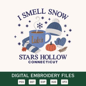 Può includere: Un disegno per ricamo con una tazza blu con la scritta Luke's, una sciarpa a righe blu e bianche, un berretto blu, muffole blu e una zucca arancione. Il testo recita I SMELL SNOW STARS HOLLOW CONNECTICUT, circondato da fiocchi di neve blu scuro.