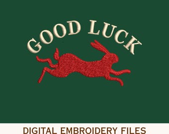 May include: A digital embroidery design featuring a red rabbit in a leaping pose centered below the text GOOD LUCK in a cream-colored font. The design is set against a dark green background with the text DIGITAL EMBROIDERY FILES at the bottom.