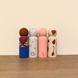 May include: Four wooden peg dolls painted with distinct designs. The first has a brown head and blue overalls over a yellow plaid shirt. The second is light grey with white cloud shapes. The third is solid pink with a small curly tail. The fourth is cream with brown spots.