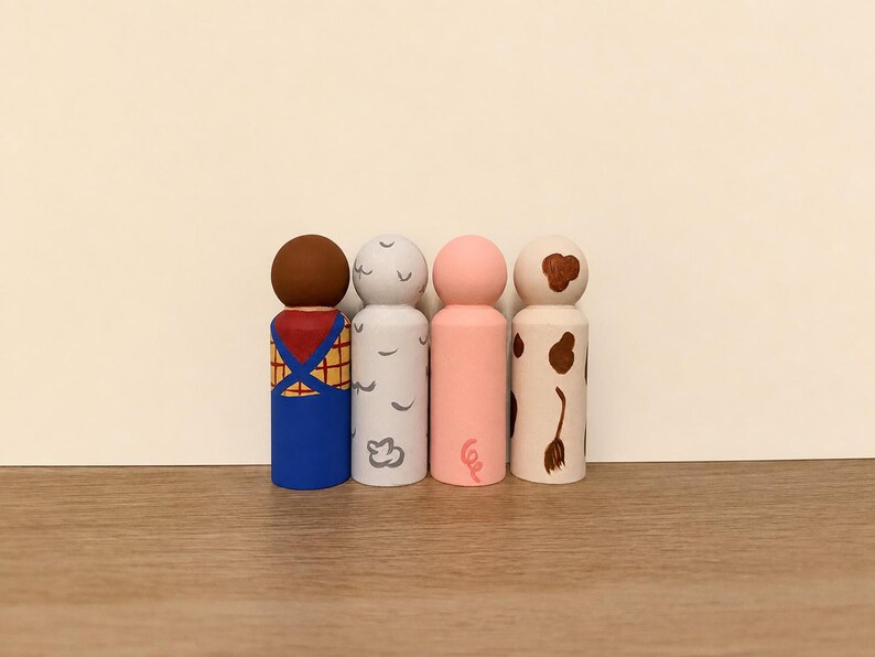 May include: Four wooden peg dolls painted with distinct designs. The first has a brown head and blue overalls over a yellow plaid shirt. The second is light grey with white cloud shapes. The third is solid pink with a small curly tail. The fourth is cream with brown spots.