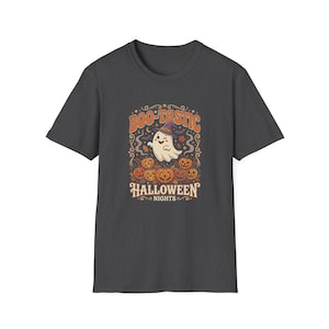 May include: A dark gray short-sleeve t-shirt featuring a graphic print of a winking ghost wearing a purple witch hat, surrounded by several orange jack-o'-lanterns and autumn leaves. The text BOO-TASTIC HALLOWEEN NIGHTS is printed in orange.