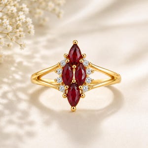 Peut inclure: Une bague en or ornée de trois pierres précieuses rouge foncé taille marquise disposées verticalement au centre, entourées de petites pierres d'accent rondes et blanches, le tout monté sur un anneau en or poli à double branche.