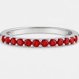 May include: A silver ring with a band of vibrant red gemstones. The gemstones are evenly spaced around the ring, creating a continuous line of color. The ring is set against a white background.