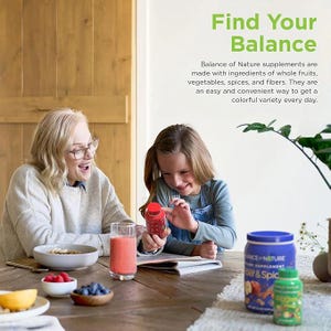 May include: An older woman and a young girl are seated at a wooden table, smiling and looking at a red bottle. A glass of pink liquid, a bowl of food, and small bowls of fruit are on the table. The text "Find Your Balance" is visible.