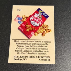 May include: A vintage Cracker Jack trading card featuring a red box of Cracker Jack popcorn and peanuts. The card has the number 23 in the upper left corner and text describing the product and manufacturer.