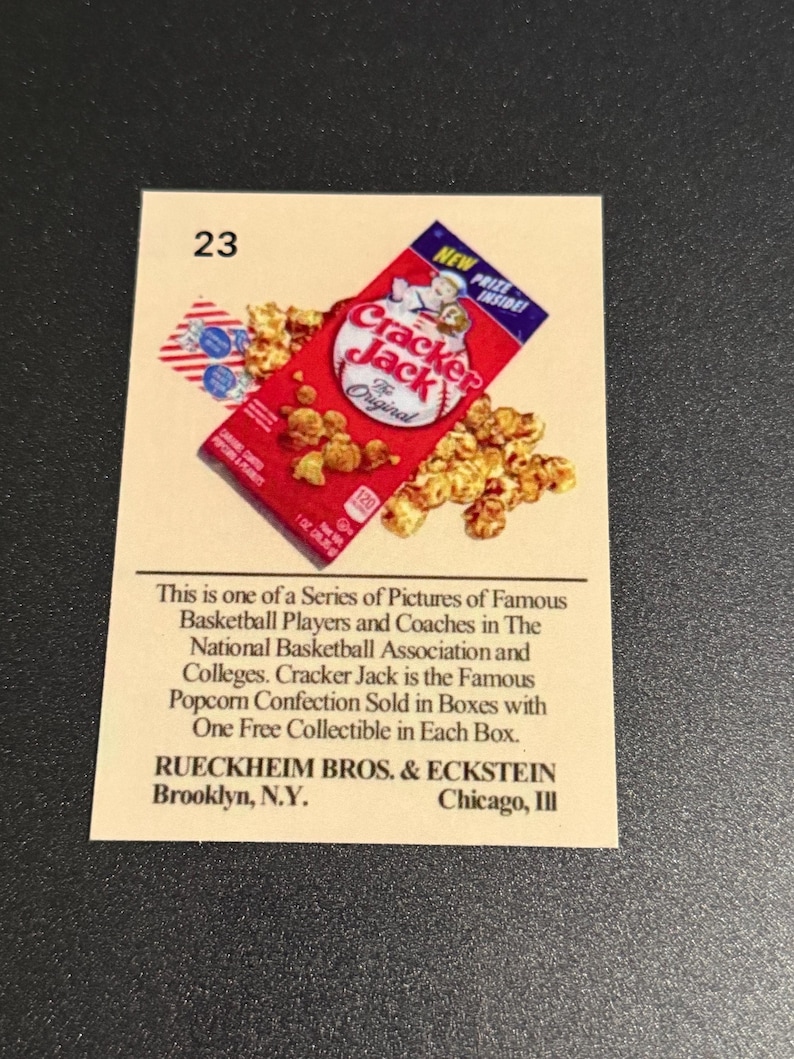 May include: A vintage Cracker Jack trading card featuring a red box of Cracker Jack popcorn and peanuts. The card has the number 23 in the upper left corner and text describing the product and manufacturer.