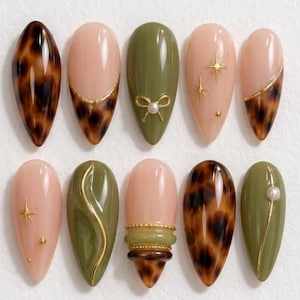 May include: A set of ten almond-shaped press-on nails featuring a mix of olive green, nude, and tortoiseshell patterns. Designs include gold star accents, a small gold bow with a pearl, gold line details, and layered bands.