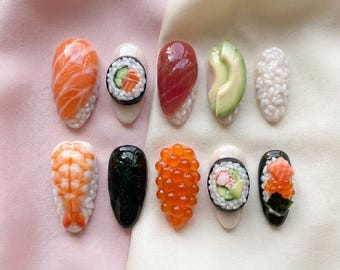 May include: A set of ten press-on nails featuring 3D sushi-themed designs. The collection includes detailed representations of salmon nigiri, tuna nigiri, avocado slices, shrimp, salmon roe, and various maki rolls with rice, cucumber, and seaweed textures.