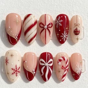 May include: A set of ten almond-shaped press-on nails featuring festive Christmas designs in red, white, and cream. Patterns include candy cane stripes, gift bows, snowflakes, a hanging ornament, and French-style tips with gold accents.