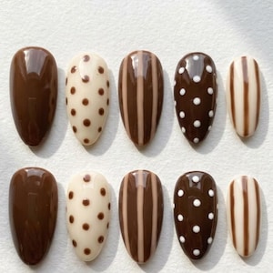 May include: A set of ten almond-shaped press-on nails featuring a glossy finish. The designs include solid dark brown, cream with brown polka dots, brown and cream vertical stripes, dark brown with white polka dots, and cream with brown stripes.