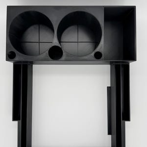 May include: A black 3D-printed desk organizer featuring two large circular cup holders, a rectangular storage compartment, and multiple narrow vertical slots for pens or tools. The structure includes additional small circular openings.