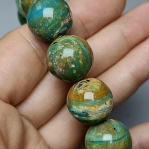 Op de afbeelding: Een armband bestaande uit gepolijste, bolvormige kralen met een gemarmerd patroon in diepe blauwgroene, bosgroene en aardse ochertinten. Elke kraal heeft een gladde, glanzende afwerking met unieke natuurlijke insluitingen en variaties.