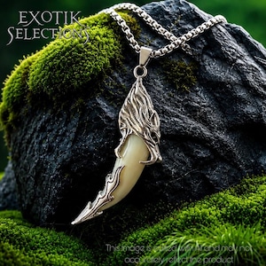 May include: A silver-toned pendant necklace featuring a curved, off-white tooth-shaped element encased in intricate, textured metal filigree. The pendant hangs from a silver-toned box chain. The text EXOTIK SELECTIONS is visible in the upper left.