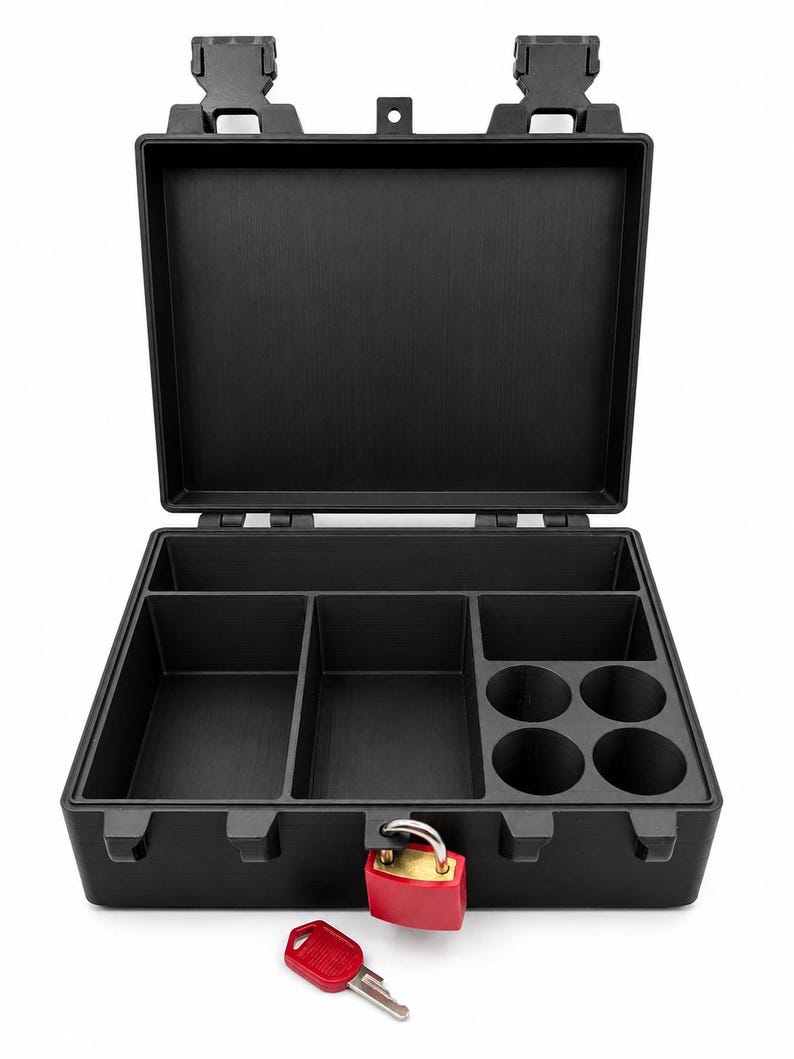 Puede incluir: Una caja de almacenamiento rectangular negra con tapa abatible abierta, que presenta m&uacute;ltiples compartimentos interiores, incluidos cuatro espacios circulares. La caja est&aacute; asegurada con un candado rojo y una llave roja a juego.