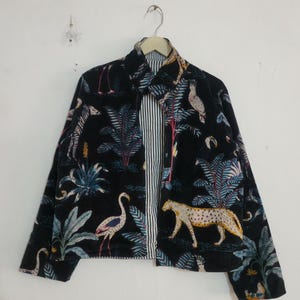 May include: A black jacket featuring a vibrant jungle print with illustrations of a leopard, a flamingo, a zebra, and tropical palm leaves. The jacket has a collared neckline, long sleeves, and a visible black and white vertical striped lining.
