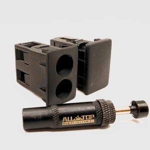 Puede incluir: Dos carcasas de interruptor rectangulares de plástico negro con aberturas circulares y una herramienta cilíndrica de metal negro con agarre moleteado. La herramienta tiene el texto blanco ALLTOP 4x4 ACCESSORIES y un pequeño émbolo de metal.