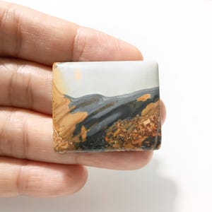 Puede incluir: Una piedra cuadrada y pulida con un diseño de paisaje. La piedra presenta una mezcla de colores, incluyendo gris, beige, marrón y blanco, creando una estética natural y terrosa. El patrón se asemeja a un paisaje en miniatura.
