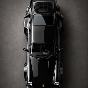 May include: Overhead view of a sleek, black Porsche Turbo sports car. The car is set against a dark gray background, with the brand name "PORSCHE" and the word "TURBO" in white lettering. The car's glossy finish reflects the light.