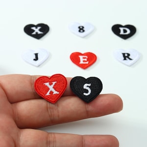 May include: A collection of heart-shaped embroidered patches featuring various letters and numbers in white thread. The patches are available in black, white, and red fabric colors, each displaying a single character centered on the heart shape.