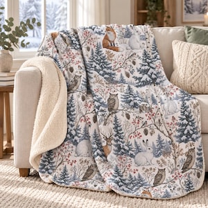 May include: A plush throw blanket featuring a winter forest scene with illustrations of foxes, rabbits, owls, and deer among snow-covered pine trees and red berry branches. The blanket has a cream-colored sherpa fleece lining.