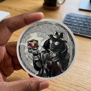 May include: A round sticker featuring a black and white illustration of a figure in a trench coat, hat, and glasses, holding a solved Rubik's Cube. The cube has colorful squares. The background has a textured, hatched design.