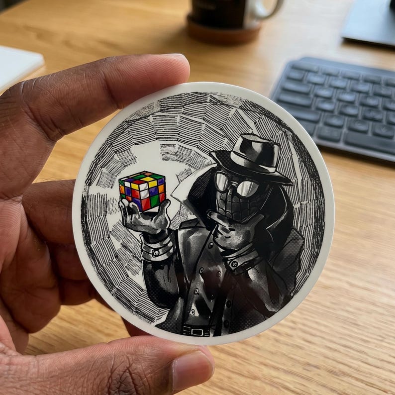 May include: A round sticker featuring a black and white illustration of a figure in a trench coat, hat, and glasses, holding a solved Rubik's Cube. The cube has colorful squares. The background has a textured, hatched design.
