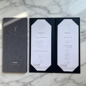 May include: A dark gray textured menu cover with a logo and the text THE ONE MANSION, alongside an open two-panel menu holder featuring white inserts with black text titled Drink List, Selection of Chinese tea, and Special Drink.