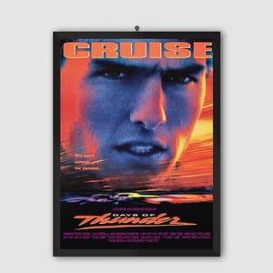 May include: Framed movie poster for "Days of Thunder" featuring a close-up of Tom Cruise's face with a blue and orange color scheme. The title is in orange, and the tagline reads "You can't outrun the thunder."