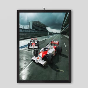 May include: Framed print featuring two Formula 1 race cars on a track. The cars are red and white with black tires, and the image is set against a cloudy sky. The print is in a black frame.