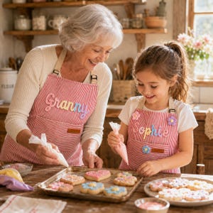 May include: Two matching red and white striped aprons, one featuring the embroidered name Granny and the other featuring the name Sophie. Both aprons have a front pocket, adjustable neck straps, and colorful flower-shaped embellishments.