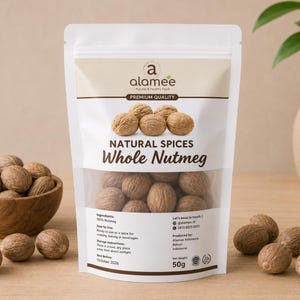 Pode incluir: Um saco branco de especiarias de noz-moscada inteira com o texto "Natural Spices Whole Nutmeg". Uma tigela de madeira cheia de noz-moscada está à esquerda. O saco contém 50g de noz-moscada. Um vaso com uma planta está ao fundo.