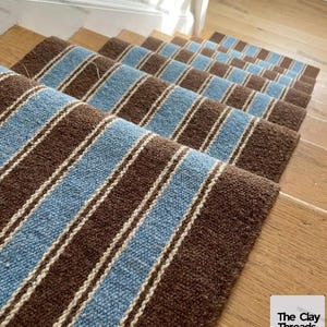 May include: A set of stair treads featuring a woven texture with alternating wide brown stripes and light blue stripes, separated by thin white pinstripes. The text "The Clay Threads." is visible in the bottom right corner of the image.