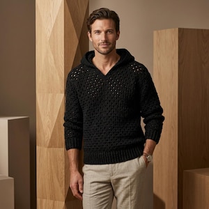May include: A black long-sleeve hooded sweater featuring an open-knit crochet pattern with a V-neckline and ribbed cuffs and hem, paired with light beige trousers. The sweater has a textured, geometric stitch design throughout the body.