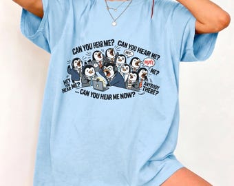 May include: A light blue t-shirt featuring a graphic of multiple penguins in business attire sitting at a computer. The text reads: CAN YOU HEAR ME? CAN YOU HEAR ME? HEY YOU HEAR ME? MUTE. ANYBODY THERE? CAN YOU HEAR ME NOW? The penguins have various expressions.