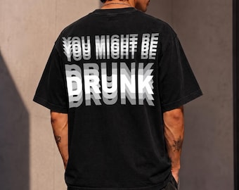 May include: A black short-sleeved t-shirt featuring a white graphic print on the back. The text reads "YOU MIGHT BE DRUNK" in a layered, motion-blur style with repeating white and grey letters creating a visual effect of movement across the fabric.