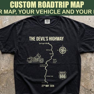May include: A black short-sleeve t-shirt featuring a white graphic of a motorcycle, a compass, and a map labeled The Devil's Highway. The design includes the text Springerville, Nutrioso, Alpine, Apache National Forest, Coronado Trail Scenic Byway, Mitchell Peak, Morenci, Route 666, and the date 27th May 2026.