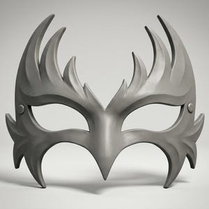 May include: A matte gray masquerade mask featuring a sharp, flame-like silhouette with pointed edges extending upward and downward. The mask includes two eye openings and a small circular rivet detail on each side near the temple area.