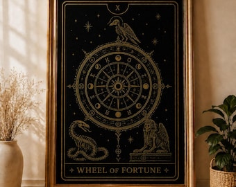 May include: A framed black and gold tarot card print featuring the Wheel of Fortune. The artwork includes a raven, snake, and sphinx, with the card's title at the bottom. The frame is a warm gold color.