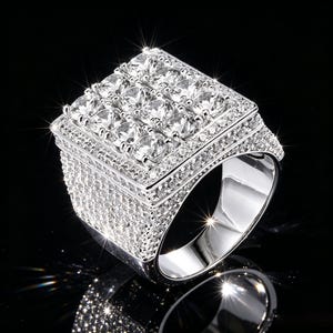 May include: A silver-toned ring featuring a large square top set with nine prominent round clear stones arranged in a grid. The entire surface of the ring, including the thick band and the square setting, is encrusted with numerous small clear stones.
