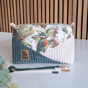 Könnte beinhalten: Rechteckige Handtasche mit Blumen- und Vogelmuster, petrolfarbenen Cord- und weißen Cordpaneelen. Die Tasche hat einen goldenen Reißverschluss und einen abnehmbaren Riemen. Der Text "be you tiful" steht auf einem braunen Etikett.