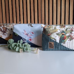 Könnte beinhalten: Drei Umhängetaschen mit einzigartigen Designs. Eine zeigt ein Blumenmuster, eine andere eine Libelle und die dritte einen Vogel- und Blumendruck. Jede Tasche hat ein kontrastierendes geometrisches Feld und einen Metallverschluss.