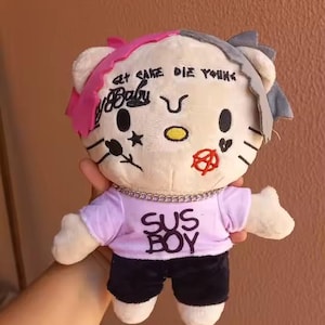 May include: A plush toy resembling a cat character with split-dyed pink and grey hair, facial tattoos including the text "GET SAKE DIE YOUNG" and "Baby", a silver chain necklace, and a light purple t-shirt with the text "SUS BOY" over black shorts.