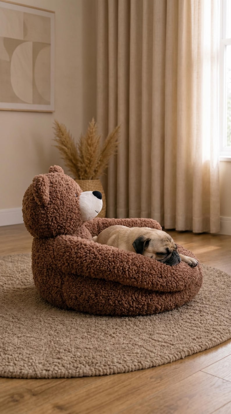May include: A brown, textured, teddy bear-shaped pet bed with a white muzzle and black nose. A small, tan pug dog is curled up and sleeping inside the soft, plush, rounded structure, which features integrated armrests and a bear head backrest.