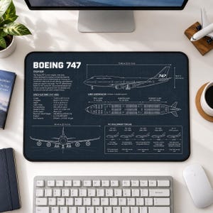 May include: A dark blue rectangular desk mat featuring a white technical blueprint of a Boeing 747 aircraft. The design includes side and top profile views, a cabin configuration layout, a development timeline, and detailed specifications in English.