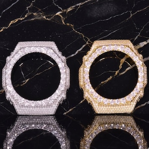 May include: Two circular watch bezels, one in silver-tone and one in gold-tone, both fully encrusted with small, clear, sparkling stones. The bezels feature a distinct octagonal outer edge and a smooth, circular inner opening for a watch face.