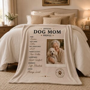 May include: A beige fleece blanket featuring the text "OFFICIAL DOG MOM PROFILE" with personalized fields including name, dog's name, best friend since, favorite activity, superpower, weakness, status, and a photo of a person holding a white dog.