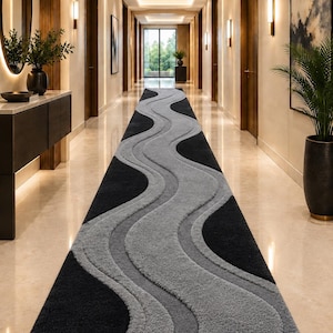 May include: A long rectangular runner rug featuring a high-low pile texture with a repeating wave pattern in contrasting shades of charcoal black and light gray, extending across the floor of a brightly lit hallway with polished light-colored flooring.
