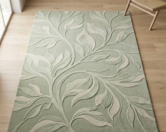 Puede incluir: Una alfombra rectangular con fondo verde salvia y un patrón botánico de hojas en relieve de color crema. El diseño consiste en enredaderas y follaje fluidos e interconectados que crean una apariencia texturizada y tridimensional.